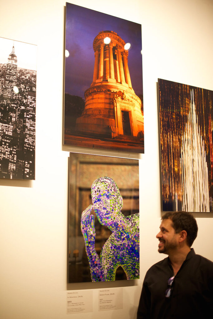 Aaron Sylvan looking his two photos on exhibit at Baboo Gallery for the 9/11 show (images are the blue figure and the orange building)